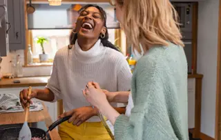 Due amiche ridono e si divertono a cucinare insieme in un'accogliente cucina.