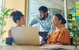 Un team che collabora in un ufficio moderno, discutendo di idee circondato da piante e foglietti adesivi colorati.