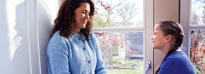 Eine Frau sitzt mit einem jungen Mädchen auf einer Fensterbank und tröstet sie.