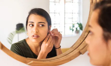 Eine junge Frau betrachtet ihr Piercing am Ohr im Spiegel.