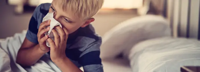 Blonder Junge mit Taschentuch auf der Nase