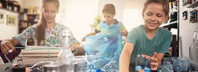 Tre ragazzini smistano carta e bottiglie di plastica in una stanza luminosa.