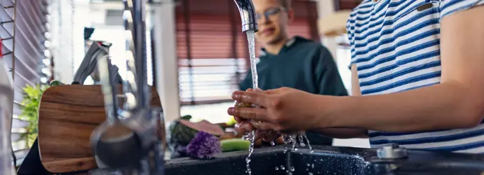 Dei ragazzini lavano delle verdure fresche nel lavandino di una cucina moderna.