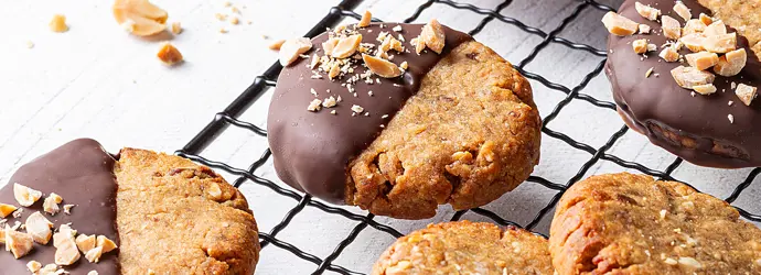 Frisch gebackene Erdnuss-Dattel-Kekse mit Schokoladenguss und Erdnuss Stückchen liegen auf einem Auskühlgitter.