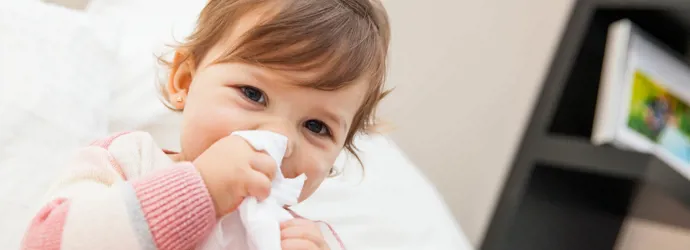 Ein kleines Mädchen putzt sich mit einem Taschentuch die Nase