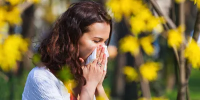 Frau mit Pollenallergie und Erkältung niest im Freien in ein Taschentuch