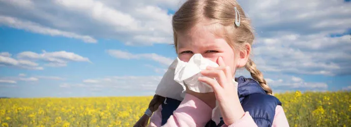 Ein junges Mädchen, das von einer Kreuzallergie betroffen ist, putzt sich in einem Feld die Nase