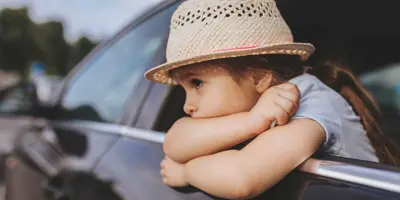 Ein Kind, dem beim Autofarhen übel geworden ist lehnt sich aus dem Autofenster