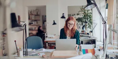 Eine Frau arbeitet an ihrem Laptop und sitzt an einem Schreibtisch