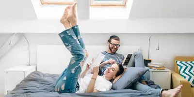 Ein junges Paar sitzt lesend auf einem Bett in einem Zimmer mit zwei Deckenleuchten