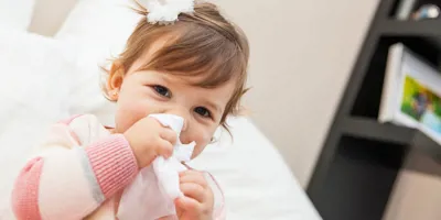 Ein kleines Mädchen putzt sich mit einem Taschentuch die Nase