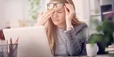 Eine junge Frau leidet unter tränenden Augen während sie an einem Laptop arbeitet