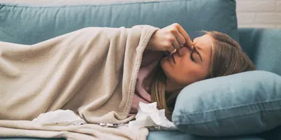 Eine Frau mit Nasennebenhöhlenentzündung liegt auf einem blauen Sofa