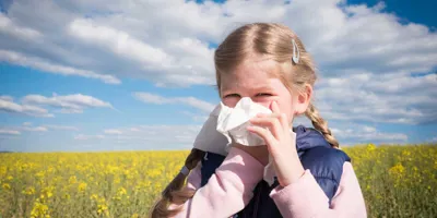 Ein junges Mädchen, das von einer Kreuzallergie betroffen ist, putzt sich in einem Feld die Nase