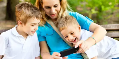 Eine Frau sitzt zwischen zwei kleinen Jungen und zeigt ihnen etwas auf dem Handy