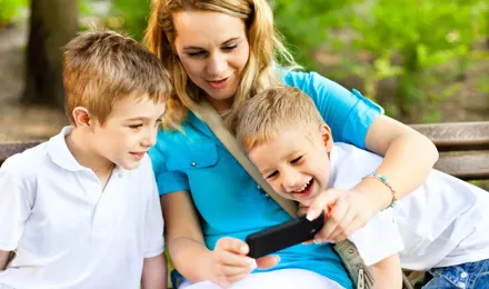Eine Frau sitzt zwischen zwei kleinen Jungen und zeigt ihnen etwas auf dem Handy