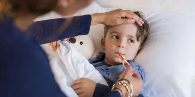 Een kind ligt in bed met een knuffel terwijl een van zijn ouders zijn externe en interne temperatuur opneemt