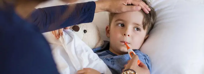 Een kind ligt in bed met een knuffel terwijl een van zijn ouders zijn externe en interne temperatuur opneemt