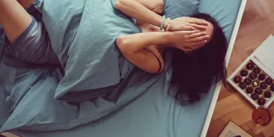 Een vrouw ligt op bed met een kussen op haar buik en haar handen voor haar gezicht