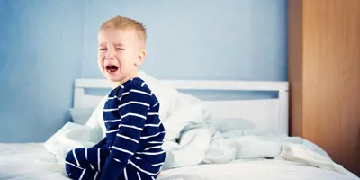 Een jong kind zit op een onopgemaakt bed te huilen