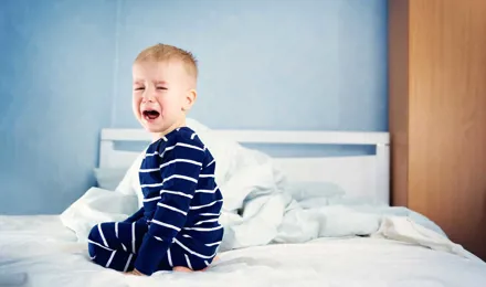 Een jong kind zit op een onopgemaakt bed te huilen