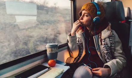 Een vrouw gekleed in winterkleding met print kijkt uit een raam van de trein terwijl ze een koptelefoon draagt