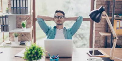 Een zeer ontspannen man leunt achterover in een stoel achter een bureau in een modern kantoor met zijn handen achter zijn hoofd