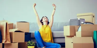Een vrouw zit te vieren op de vloer van een leeg huis, omgeven door volle kartonnen dozen