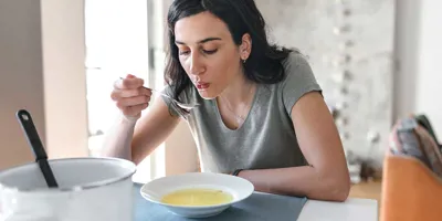 Eine Frau mit dunklen Haaren isst zu Hause eine Brühe als Heilmittel gegen Schnupfen