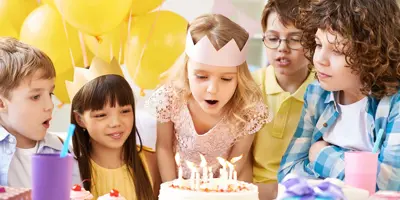 Gruppe junger Kinder an einem Tisch mit Luftballons, Kuchen auf einer Geburtstagsparty für Kinder