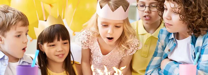 Gruppe junger Kinder an einem Tisch mit Luftballons, Kuchen auf einer Geburtstagsparty für Kinder