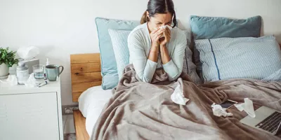 Eine Frau putzt in einem Bett ihre Nase mit einem Taschentuch