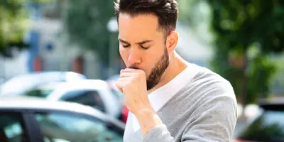 Ein Mann hustet während er von Autos umgeben ist