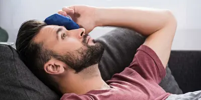 Man in bed legt een kompres op zijn ogen