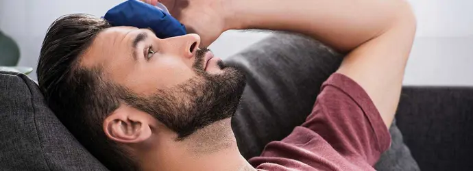 Man in bed legt een kompres op zijn ogen