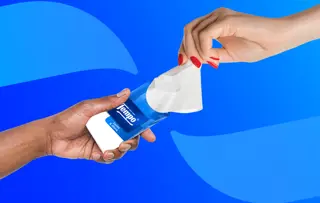 Twee handen wisselen een pakje Tempo-tissues uit tegen een blauwe achtergrond met abstracte gebogen vormen