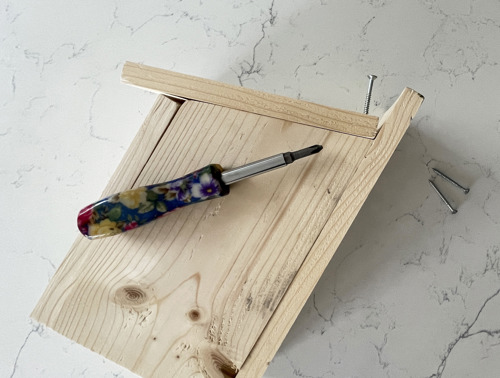 Casetta per uccelli in legno parzialmente assemblata con cacciavite e viti vicine.