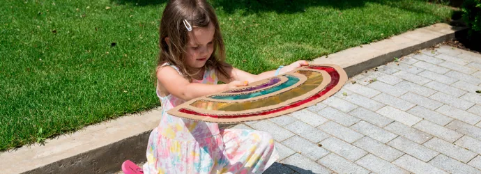 Ein Mädchen in einem geblümten Kleid betrachtet den Schatten eines selbst gebastelten Sonnenfängers auf dem Boden.