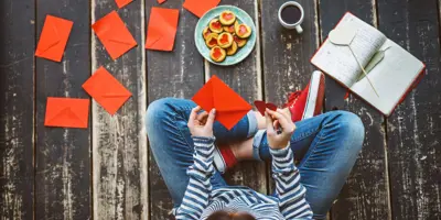 Eine Frau sitzt auf dem Boden und schreibt Karten als selbstgemachtes Geschenk für Valentinstag