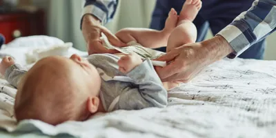 Ein Baby mit Windelausschlag wird auf einer weichen Unterlage gewickelt und frisch angezogen.