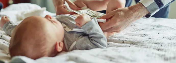 Ein Baby mit Windelausschlag wird auf einer weichen Unterlage gewickelt und frisch angezogen.