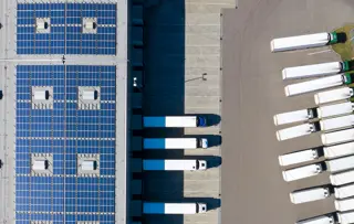Vista dall'alto di un magazzino con pannelli solari sul tetto e una flotta di camion parcheggiati sotto.