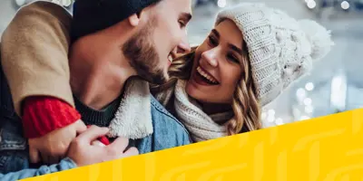 Afbeelding van een stel in winterkleding dat elkaar omhelst, met daaroverheen een diagonaal geel Tempo-patroon in de rechterhoek.