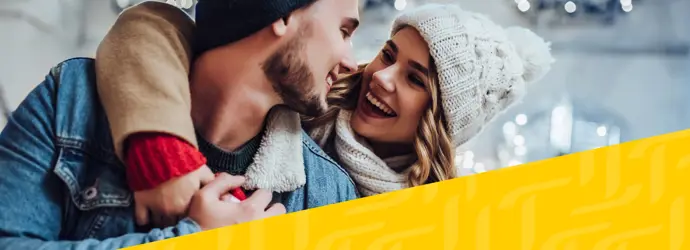 Afbeelding van een stel in winterkleding dat elkaar omhelst, met daaroverheen een diagonaal geel Tempo-patroon in de rechterhoek.
