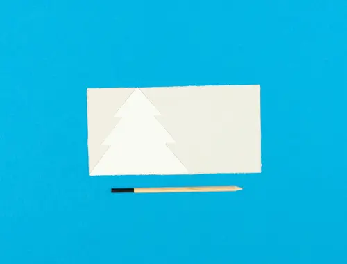 Un albero di Natale è sovrapposto su un foglio rettangolare color crema, in basso un paio di forbici tutto su sfondo blu.