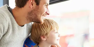 Ein Mann sitzt mit einem Kind in einem Bus und beide sehen lächelnd aus dem Fenster.