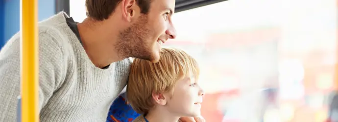 Ein Mann sitzt mit einem Kind in einem Bus und beide sehen lächelnd aus dem Fenster.