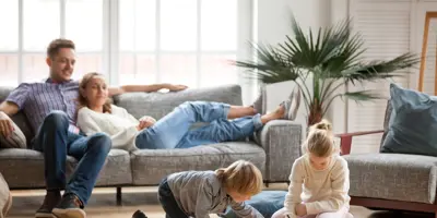 Ein Paar sitzt zusammen auf einer Couch, während es zwei Kindern beim Spielen zusehen.