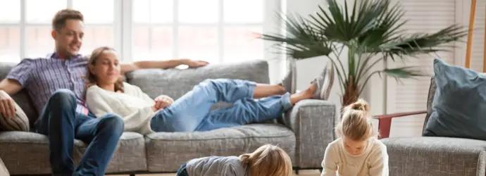 Ein Paar sitzt zusammen auf einer Couch, während es zwei Kindern beim Spielen zusehen.