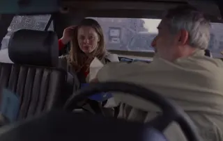 Een grijsharige taxichauffeur biedt een Tempo-zakdoekje aan een jonge vrouw die huilend op de achterbank zit